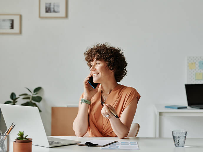 Frau telefoniert in Büro oder Arbeitszimmer, vor ihr ein aufgeklappter Laptop