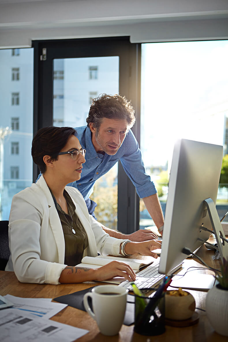 Mann und Frau schauen gemeinsam auf einen Monitor in einem modernen Büro